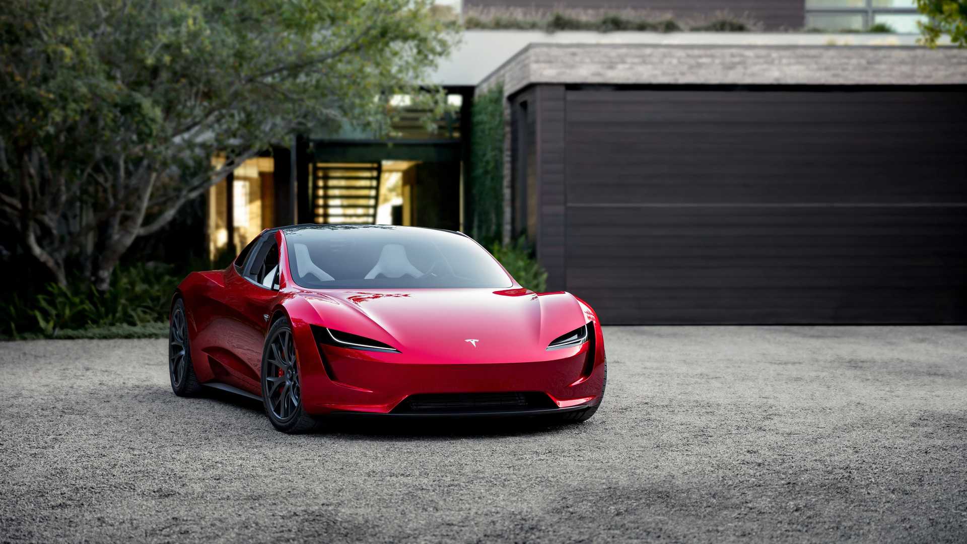 نمای جلو خودروی الکتریکی تسلا رودستر / Tesla Roadster قرمز رنگ در کنار خانه و درخت